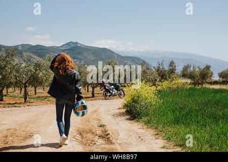 Back view of redheaded motorcyclist walking on dirt track, Andalusia, Spain Stock Photo