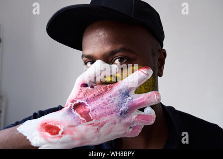 Angry artist with hand covered in paint looking at camera Stock Photo