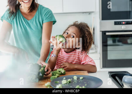 Girl cooking with mother in kitchen tasting broccoli Stock Photo