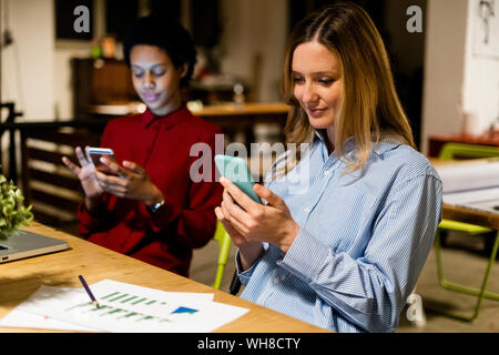 Two businesswomen using cell phones at desk in office Stock Photo