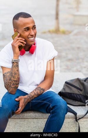 Portrait of tattooed young man on the phone sitting on bench Stock Photo