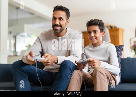 Happy father and son playing video game on couch in living room Stock Photo