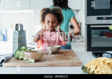 Girl playing with grated cheese in kitchen Stock Photo