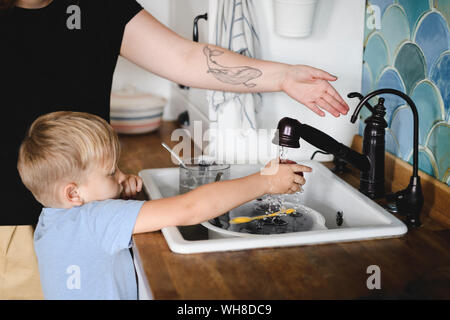 Little boy washing peach in the kitchen with his mother's help Stock Photo