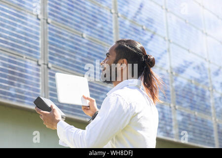 Bearded young man measuring photovoltaic plant on house facade Stock Photo