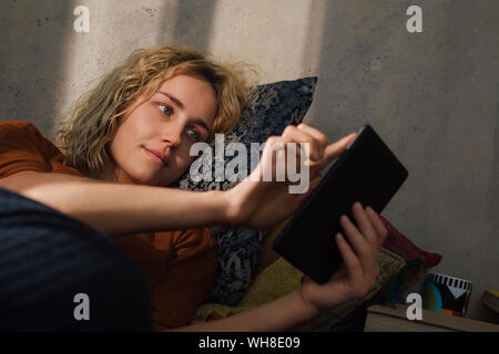 Portrait of young woman lying on bed using E-book reader Stock Photo