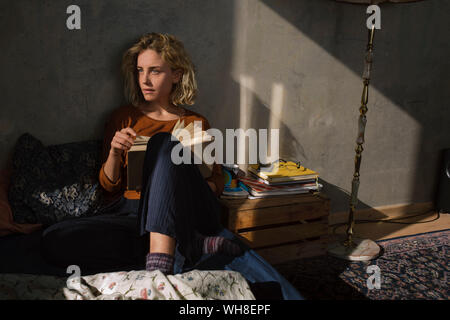 Pensive student sitting on bed with a  book Stock Photo