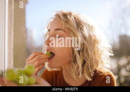 Portrait of blond young woman eating green grapes Stock Photo