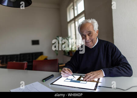 Portrait of smiling senior man using tablet with architectural plan Stock Photo