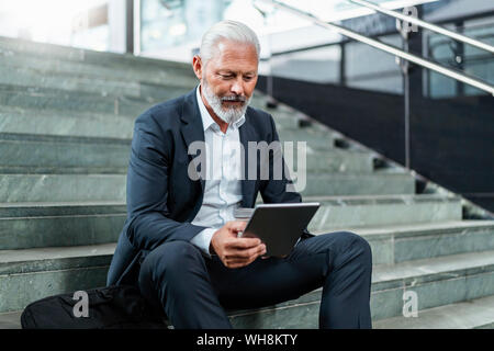 Mature businessman sitting on stairs using tablet Stock Photo