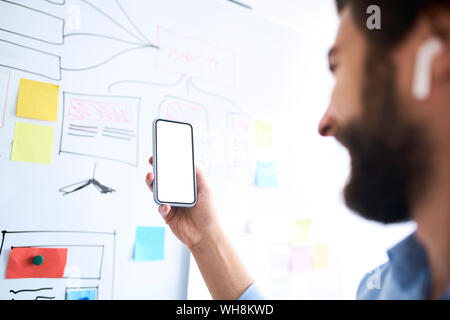 Businessman standing in front of a whiteboard and holding aloft his smartphone Stock Photo