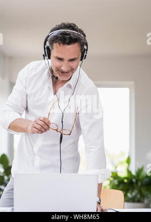 Businessman in bright office having conference call, using headset and laptop Stock Photo