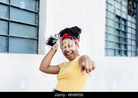 Portrait of excited young woman listening music with headphones and earphones in front of white wall Stock Photo