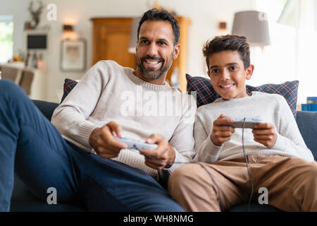 Happy father and son playing video game on couch in living room Stock Photo