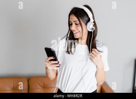 Happy young woman with smartphone and headphones at home Stock Photo