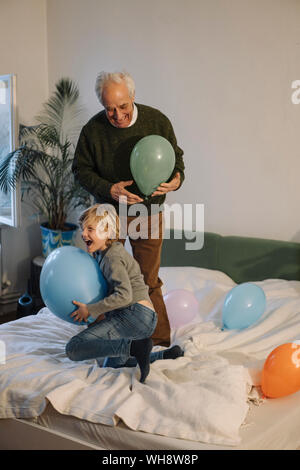 Happy grandfather and grandson playing with balloons on bed at home Stock Photo