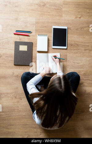 Top view of young woman sitting on the floor at home taking notes Stock Photo