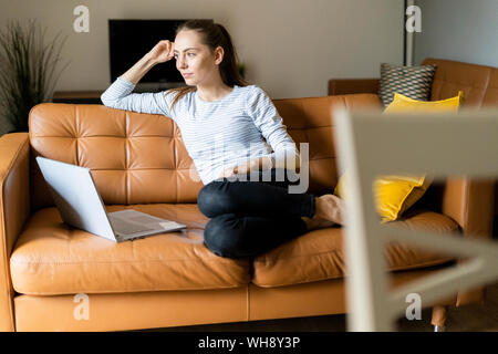 Young woman sitting on couch at home with laptop