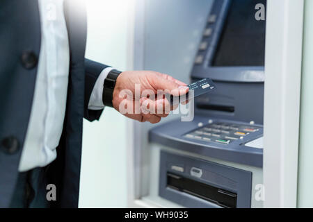 Mature businessman withdrawing money with credit card at an ATM Stock Photo