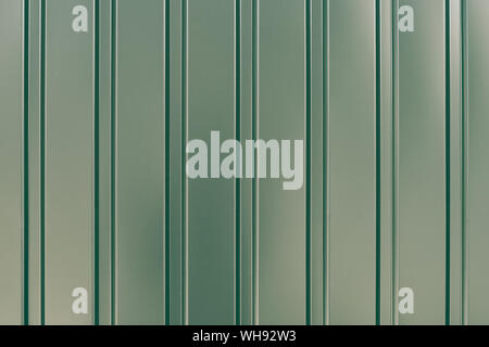 Green metallic striped surface. Metal wall siding. Striated fence with shine. Convex wall texture. Ribbed surface. Shiny metallic cladding. Reflected Stock Photo