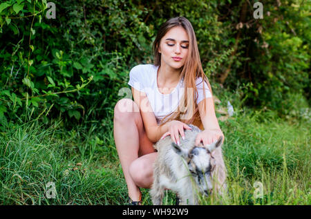Woman play cute goat. United with nature. Animals law. Girl and goat green grass. Farm and farming concept. Village animals. Protect animals. Veterinarian occupation. Treating animals at farm. Stock Photo