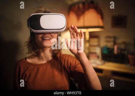 Young woman using Virtual Reality Glasses at home Stock Photo