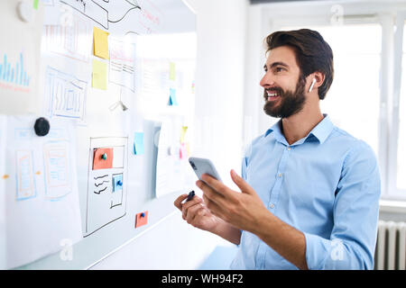 Businessman standing in front of a whiteboard and using his smartphone Stock Photo