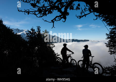 Mountain bikers look out across a valley filled with a cloud inversion in the Himalayas while biking in the Gosainkund region, Langtang region, Nepal Stock Photo