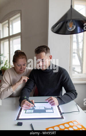 Senior woman watching man using tablet with architectural plan Stock Photo