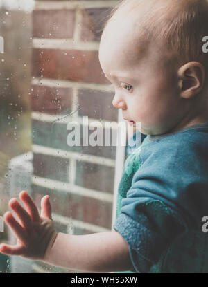 Baby girl looking through window covered with raindrops Stock Photo