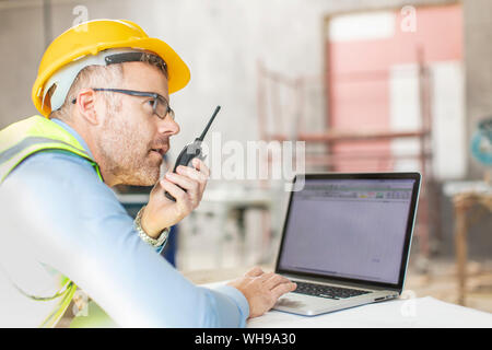 Architect using laptop and walkie talkie at construction site Stock Photo