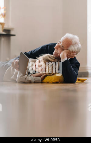 Happy grandfather and grandson lying on the floor at home using a tablet Stock Photo