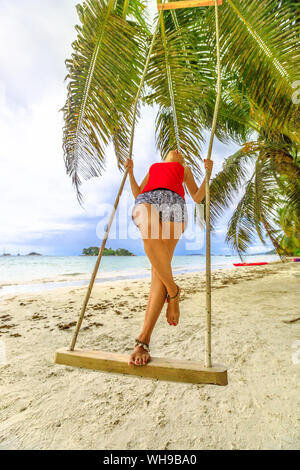 Woman swinging on tropical beach of Anse Volbert with Islet of Chauve Souris in the background, Cote d'Or, Praslin, Seychelles Stock Photo