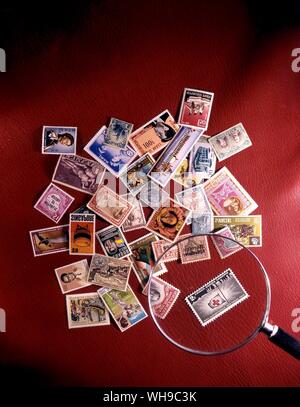 A number of stamps from all over the world stacked randomly in a pile with a magnifying glass on a red background. Stock Photo