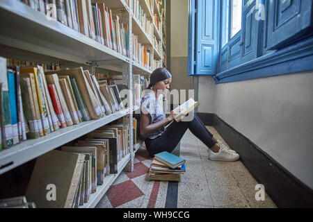 Young woman sitting on the floor reading a book at National library, Maputo, Mocambique