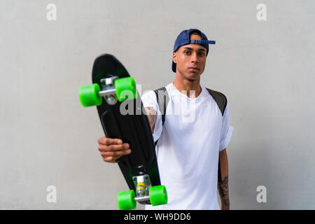 Portrait of tattooed young man with skateboard in front of grey background Stock Photo