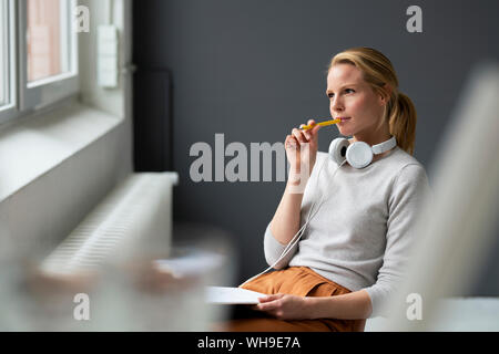Young woman sitting on chair at the window in office thinking Stock Photo