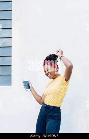 Young woman listening music with headphones and earphones singing and dancing in front of white wall Stock Photo