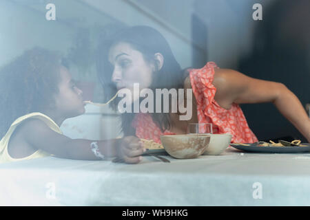 Mother and daughter eating pasta at dining table sharing a spaghetti Stock Photo