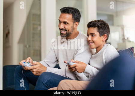 Happy father and son playing video game on couch in living room Stock Photo