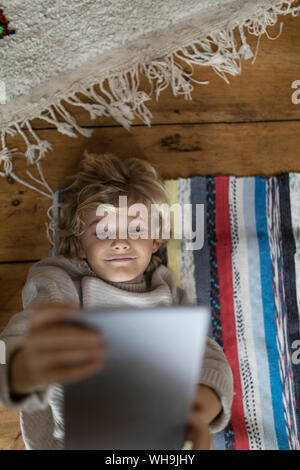 Top view of boy lying on carpet using tablet Stock Photo