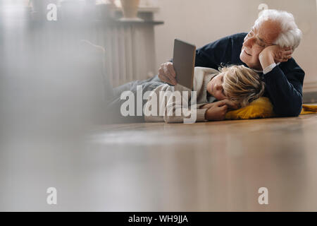 Grandfather and grandson lying on the floor at home using a tablet Stock Photo