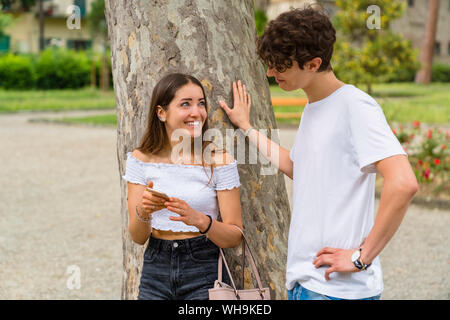 Young couple in a park, woman showing him her smartphone and smiling Stock Photo