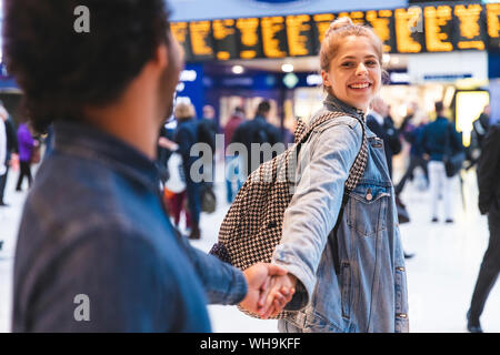 Portrait of happy young woman hand in hand with his boyfriend at train station Stock Photo