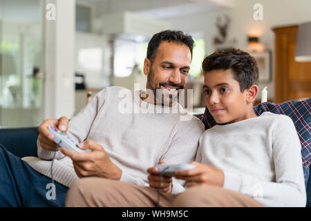 Happy father and son playing video game on couch in living room Stock Photo