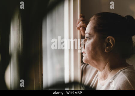 Serious senior woman looking out of window at home Stock Photo
