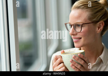 Young businesswoman with cup of coffee looking out of window Stock Photo