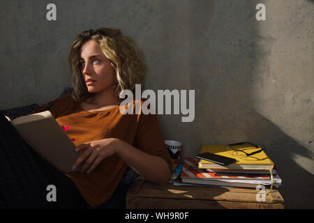 Pensive student sitting on bed with a book Stock Photo