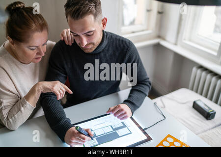 Senior woman watching man using tablet with architectural plan Stock Photo