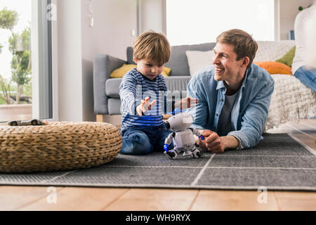 Father and son lying on floor, playing with toy robot Stock Photo
